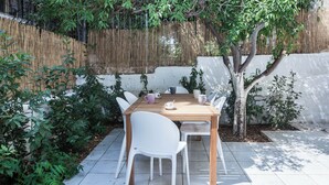 A wooden table with white chairs, surrounded by plants and a bamboo fence. - Cozy 1 Bd Basement Apt in Pagrati (Athens)
