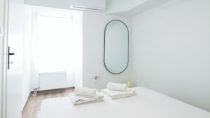 A hotel room with a bed, two towels, a round mirror, an air conditioning unit, and a radiator. - Cozy 1 Bd Basement Apt in Pagrati (Athens)