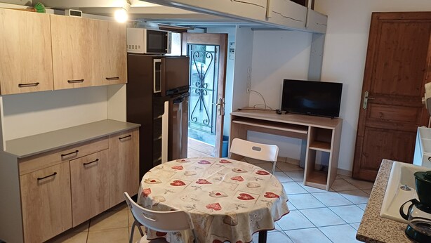 Una cucina funzionale con tavolo, sedie, frigorifero, forno a microonde e televisore su un mobile in legno.