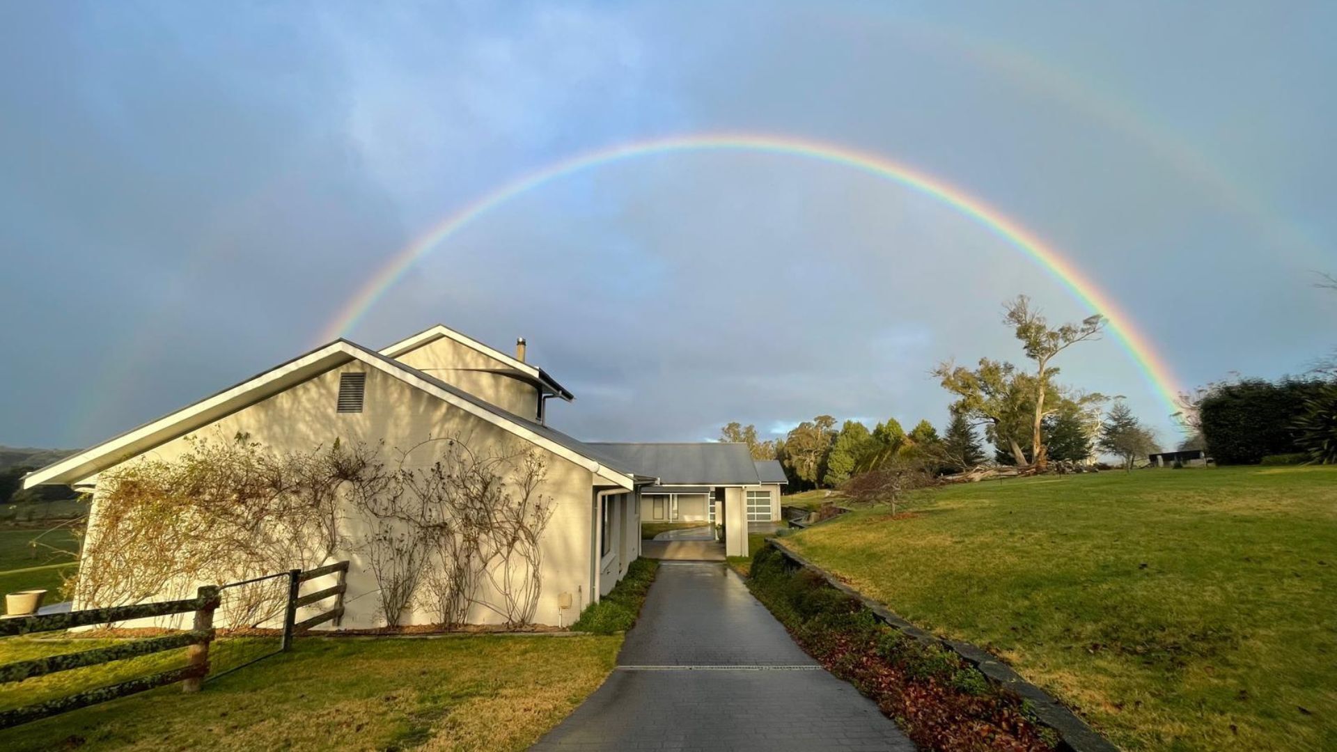 A building with a sloped roof, a pathway leading to it, and a rainbow in the background.