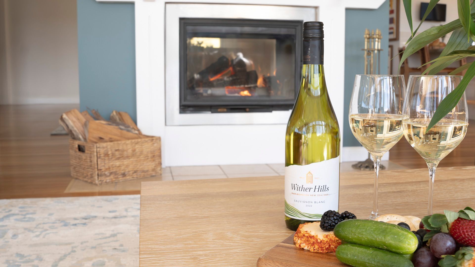 Eine Flasche Wither Hills Sauvignon Blanc 2022, zwei Weingenüge und ein Holzschneidebrett mit Käse, Brombeeren und Gurken.