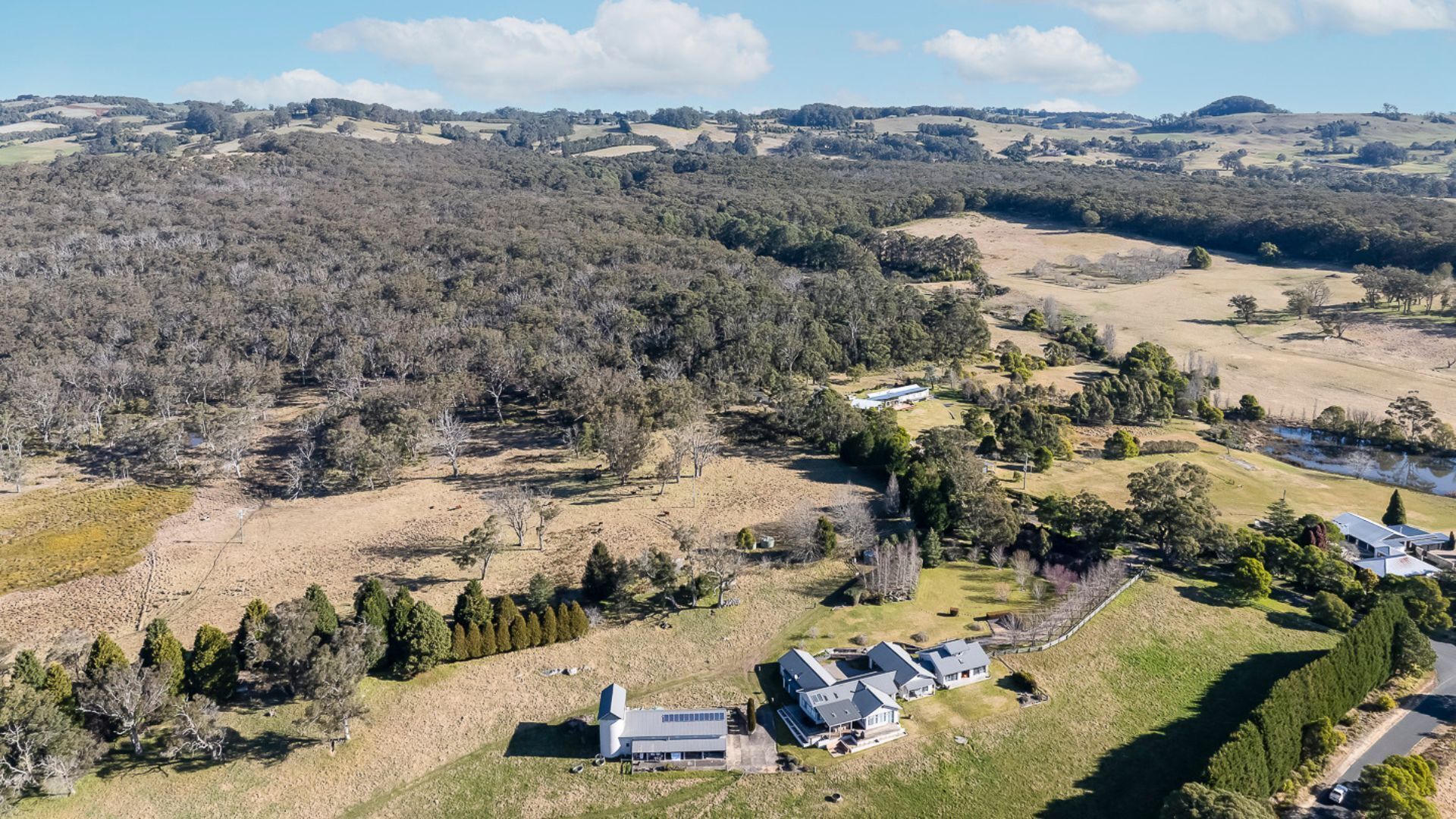 Luchtbeeld van een landgoed met een groot huis, een gastenverblijf en een zwembad, omringd door dicht bos en glooiende heuvels.
