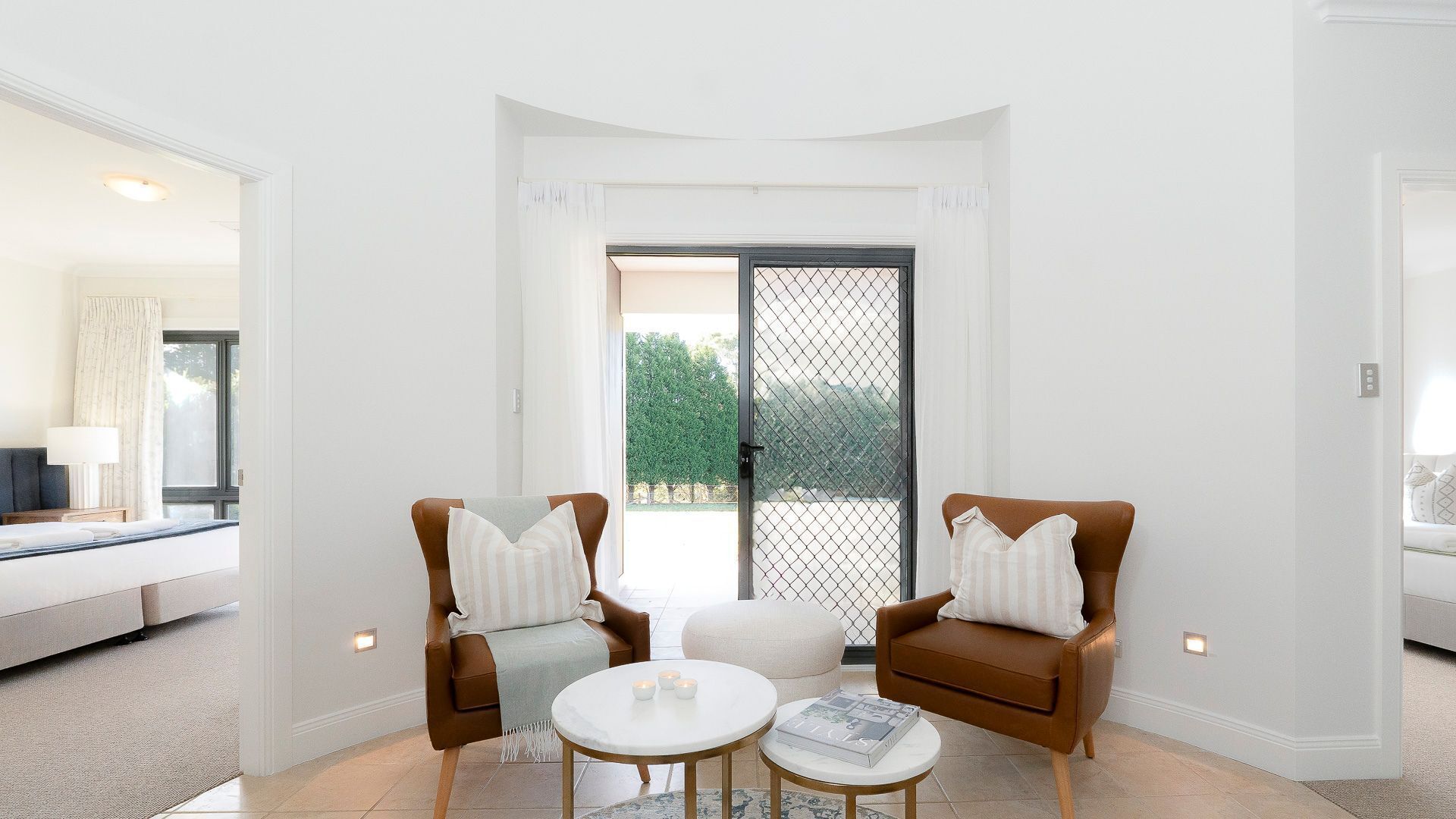 A modern living room with two brown leather armchairs, a round coffee table, and a large sliding glass door leading to an outdoor area.
