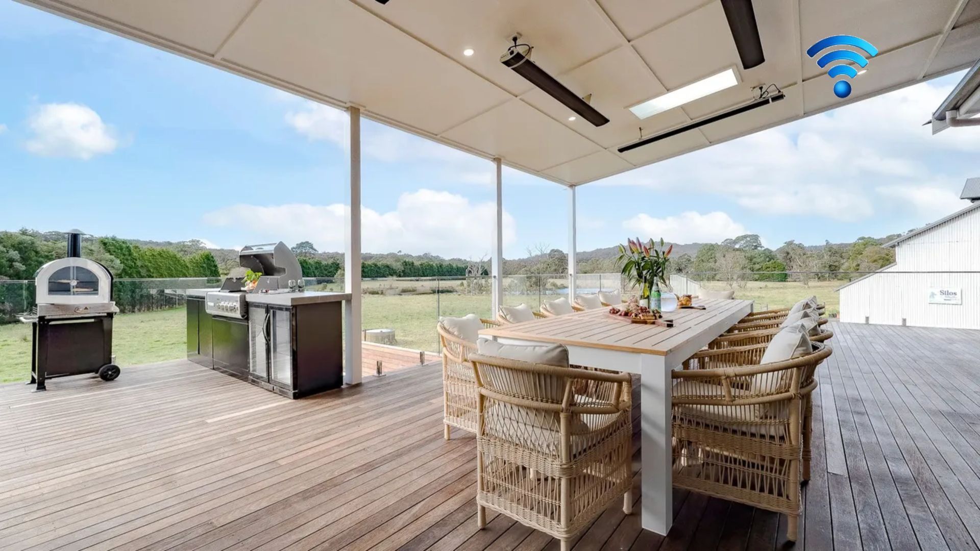 An outdoor patio with a wooden deck, a table with chairs, a grill, and a view of the landscape.