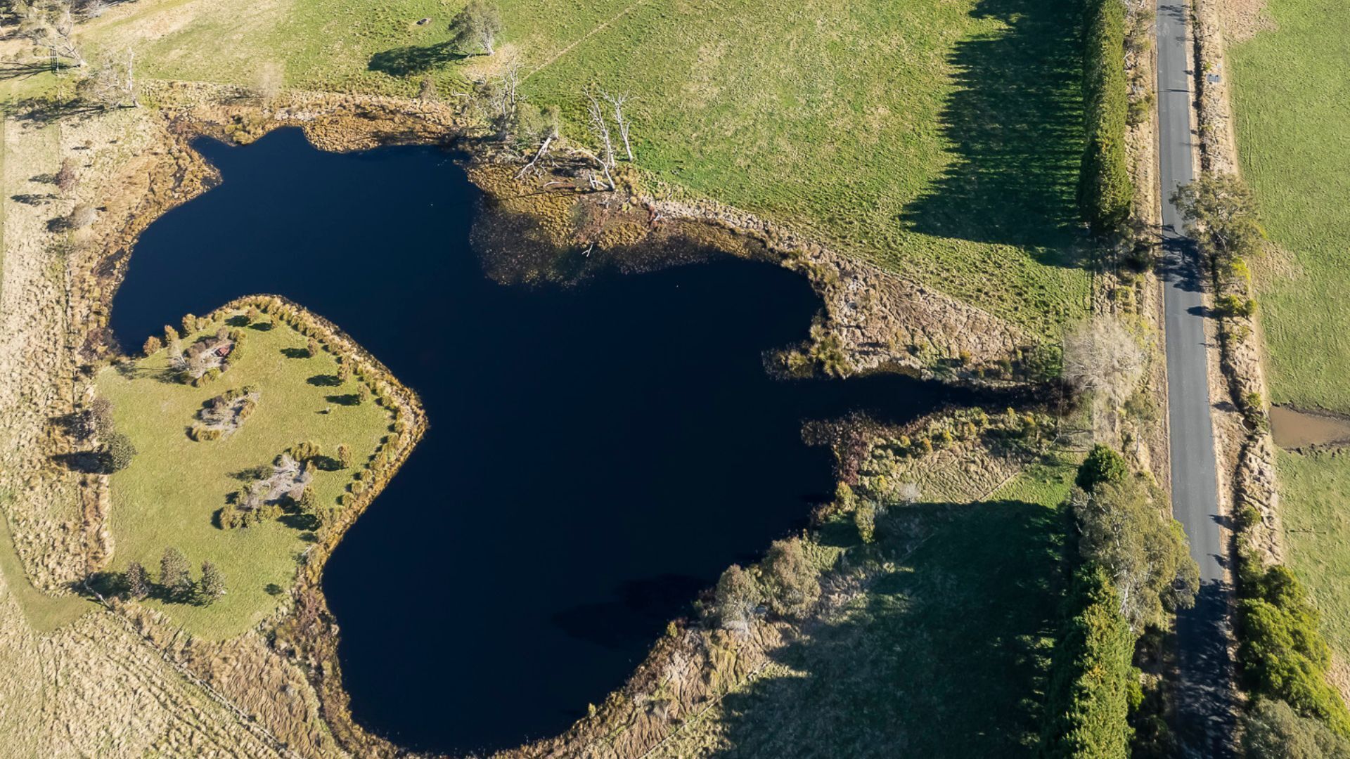 An aerial view of a lake with a small island and a road running parallel to the water's edge.