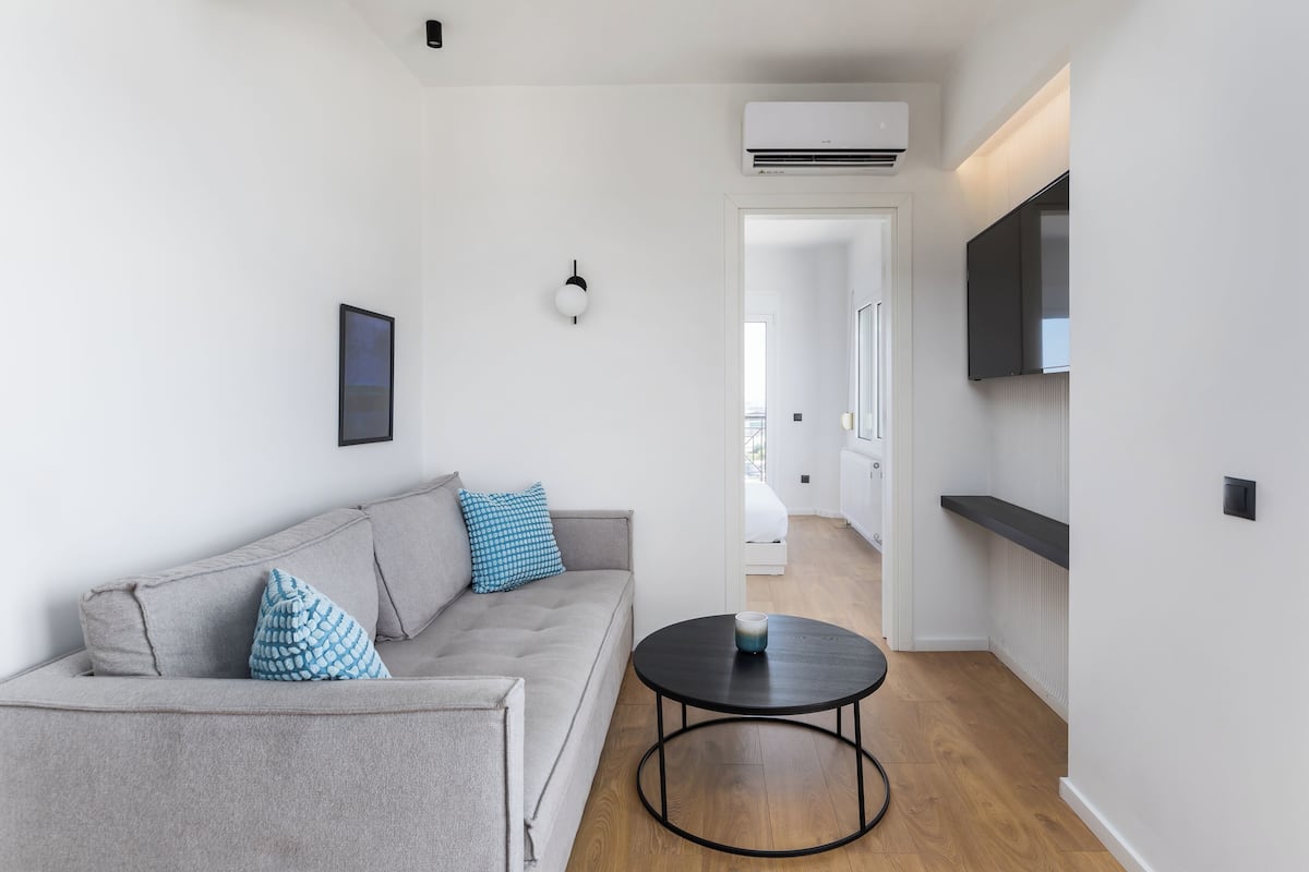 A modern living room with a grey sofa, a round black coffee table, and a flat-screen TV mounted on the wall.