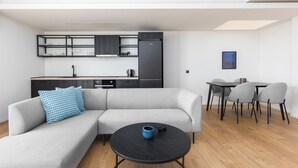 Uma sala moderna com um sofá seccional cinza, uma mesa de centro preta e um espaço de jantar com cadeiras cinzas e uma mesa preta.