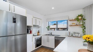 A modern kitchen with stainless steel appliances, white cabinetry, a wooden floor, and a window with a view of the sky. - Casablanca by Khove (Labrador)