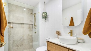 A modern bathroom with a glass-enclosed shower, a white sink, and wooden cabinets. - Casablanca by Khove (Labrador)