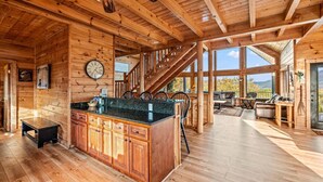 A spacious cabin interior with a wooden interior, a kitchen area with a large island, and a staircase leading to a balcony with a view.