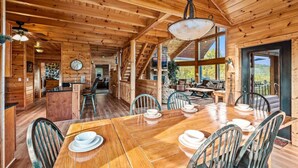 A wooden cabin interior with a dining area, kitchen, and a staircase leading to a balcony.