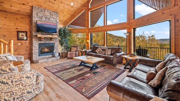 A spacious living area with a stone fireplace, leather sofas, and large windows offering a view of the outdoors.
