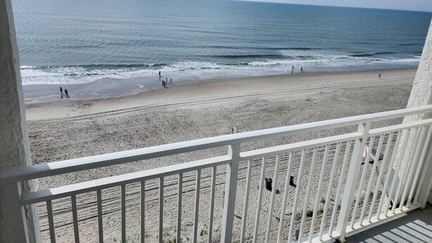 Une vue sur la plage depuis un balcon doté d’une balustrade, avec une plage de sable et l’océan en toile de fond.