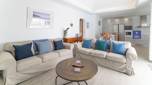 A modern living room with two beige sofas, a round coffee table, and a dining area with a table and chairs.