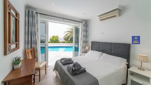 A hotel room with a bed, a desk, a chair, a nightstand, and a view of an outdoor swimming pool.