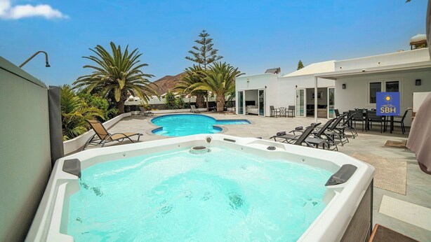 A pool area with a hot tub, lounge chairs, and a covered seating area.