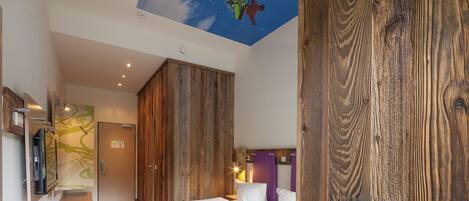 Habitación de hotel con una cama grande, armario de madera y un mural en el techo con un esquiador.