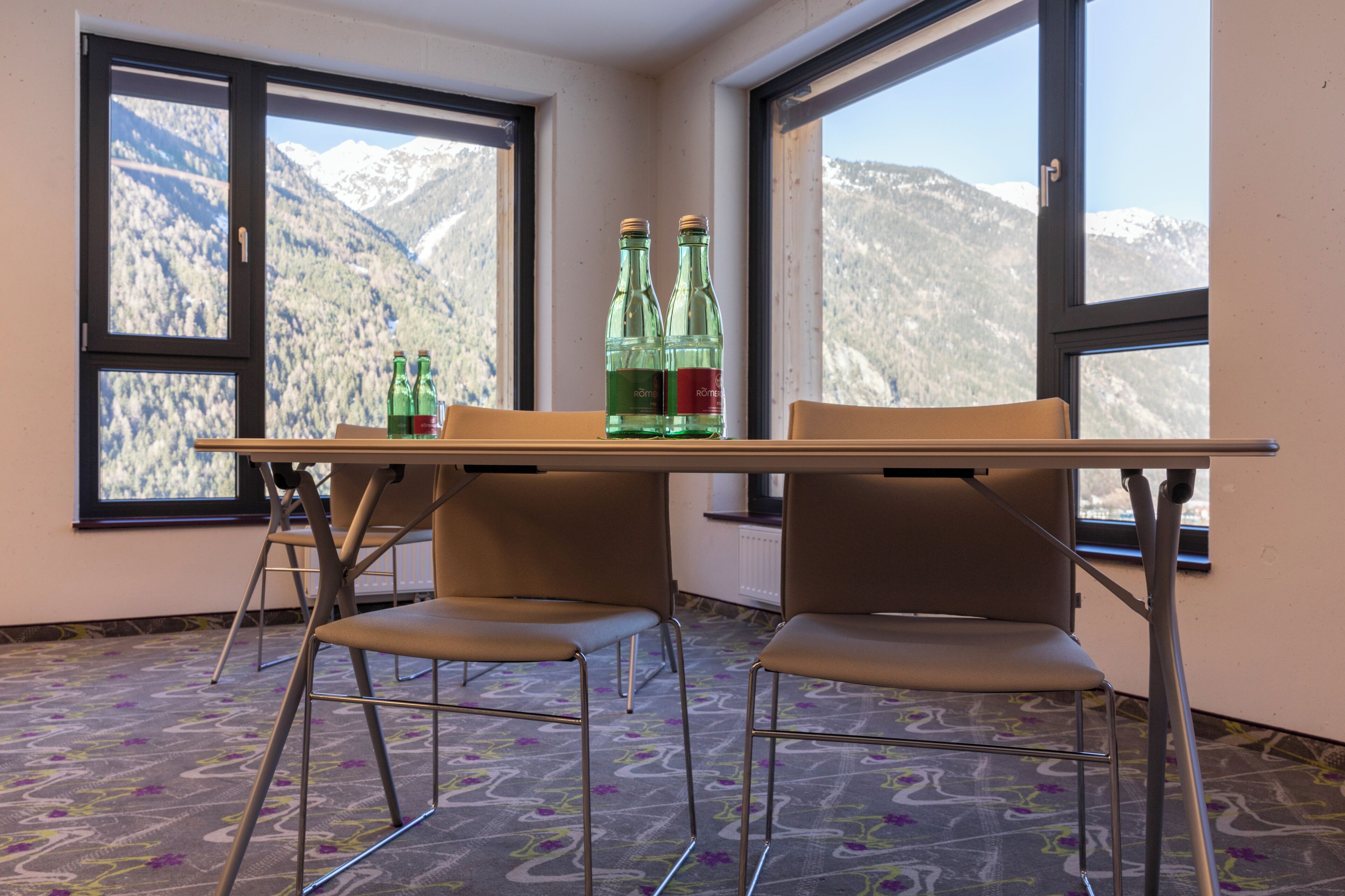 A room with a table, two chairs, and a window with a mountain view.
