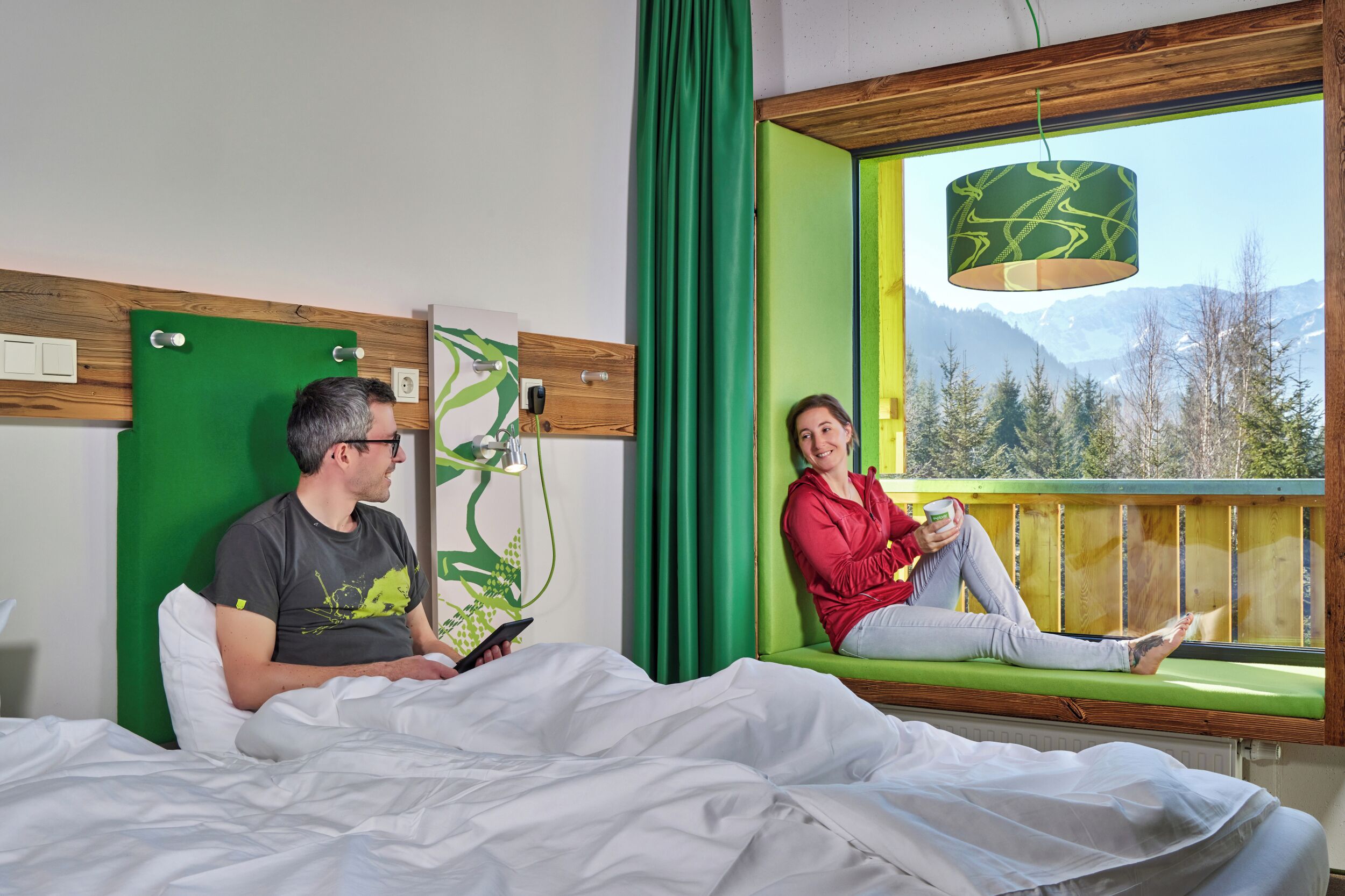 Una habitación con cama, ventana con vistas a montañas y una lámpara colgante.