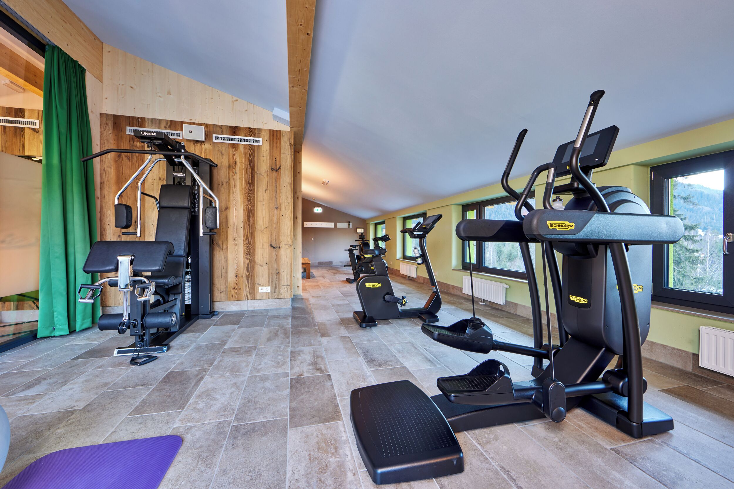 Un gimnasio con equipamiento de ejercicio, una colchoneta morada y una ventana con vistas al exterior.