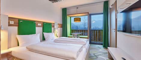 A hotel room with a bed, a desk, a chair, and a view of mountains through the window.