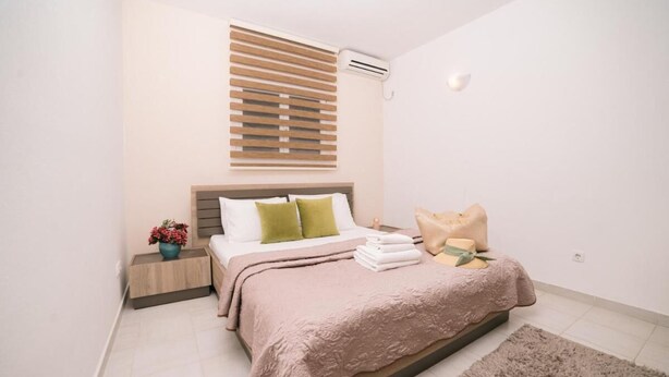 Een slaapkamer met een bed, nachtkastje, een kamerplant en een raam met luxaflex.