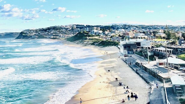 Un pueblo costero con playa, edificios y un paisaje montañoso de fondo.