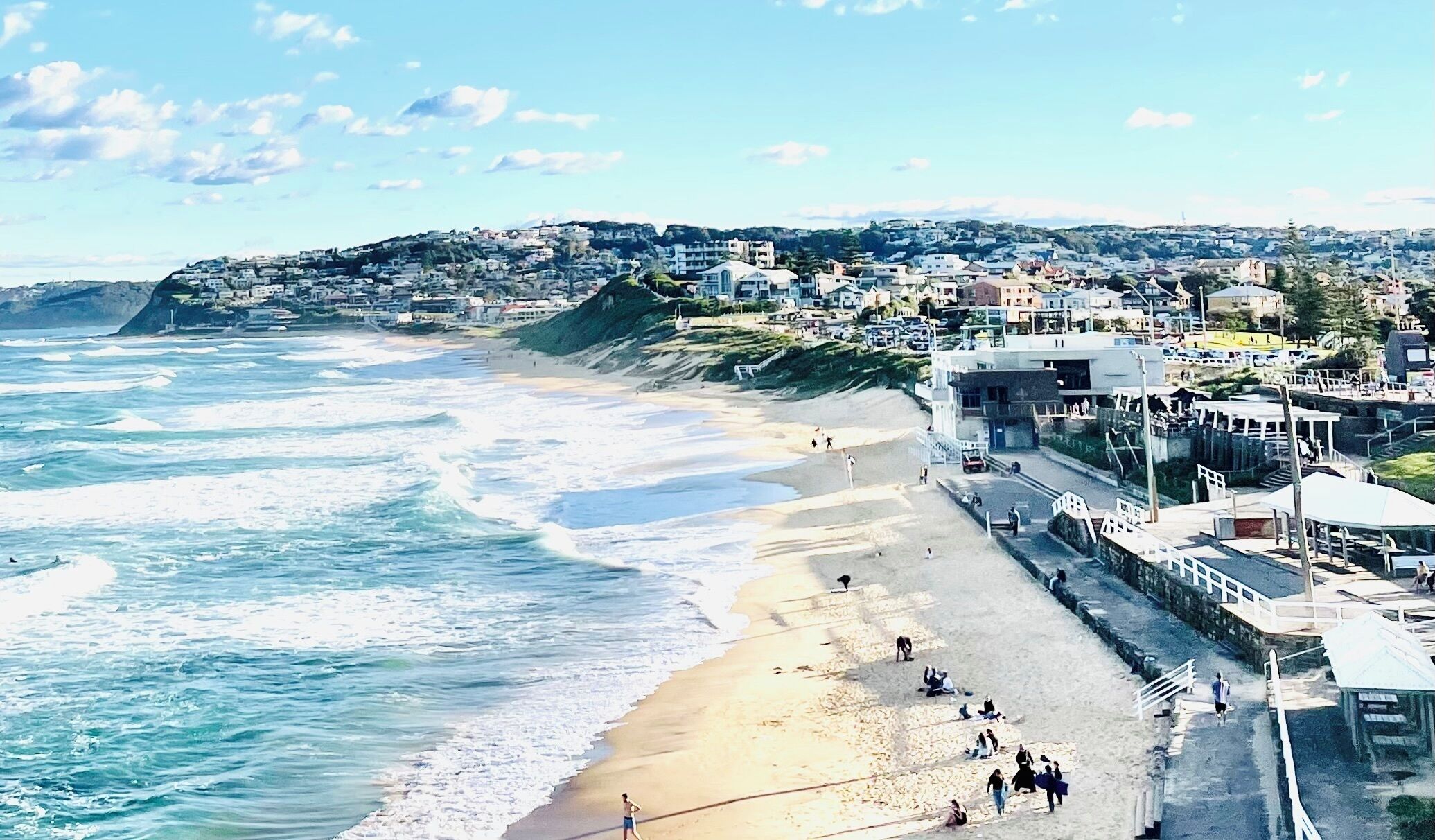 A coastal town with a beach, buildings, and a hilly backdrop. - Beautiful Bar Beach - stay 300m to Sand & Surf. Walk to Cafes & Restaurants. (Bar Beach)