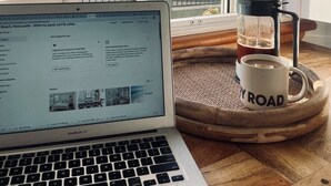Un MacBook Air sobre una mesa de madera, con una cafetera y una taza con la etiqueta "YROAD".