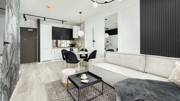 A modern living room with a white sofa, black chairs, a coffee table, and a kitchen in the background.