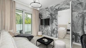 A modern hotel room with a large bed, a sitting area with a coffee table, a large mirror, and a view of the outdoors.