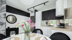 A modern dining area with a white table set for two, a vase of flowers, and a kitchen in the background.