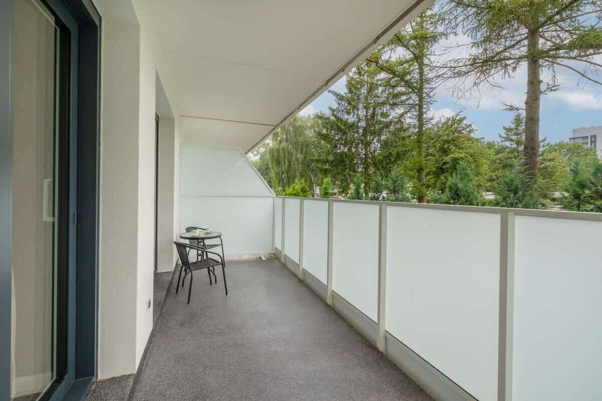 Un balcon avec une petite table et des chaises, entouré d’une balustrade blanche et de portes vitrées.