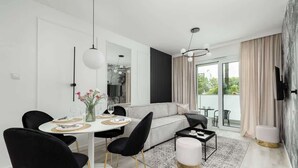 A modern living room with a white sofa, black chairs, a dining table with a vase of flowers, and a large window with curtains.