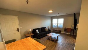 A spacious living room with a wooden dining table, a black sofa, and a coffee table. - Modern Apartment Near Aksarben Village & Dining (Omaha)