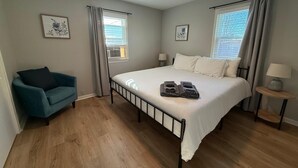 A bedroom with a bed, two bedside tables, a chair, and two windows with curtains.