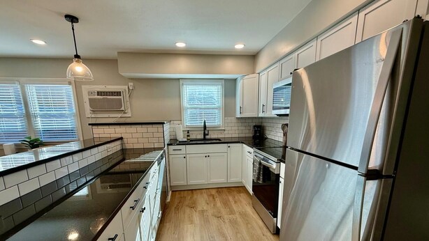 A modern kitchen with white cabinets, a stainless steel refrigerator, and a black countertop.