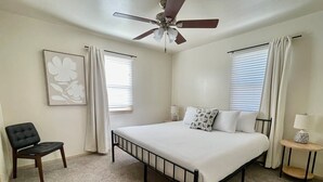 A bedroom with a bed, a chair, a nightstand, a ceiling fan, and a window with curtains. - Central Apartment by UNMC, Walk Everywhere (Omaha)