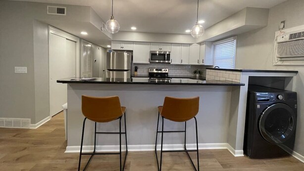 A modern kitchen with a central island, stainless steel appliances, and two bar stools. - Central Apartment by UNMC, Walk Everywhere (Omaha)
