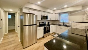 A modern kitchen with stainless steel appliances, white cabinetry, and a black countertop. - Central Apartment by UNMC, Walk Everywhere (Omaha)