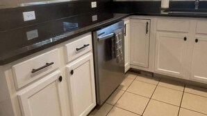 Een keuken met witte kastjes, een zwart aanrecht en een betegelde vloer.