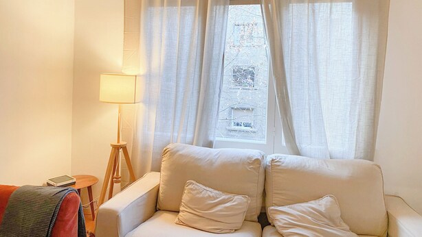 A living room with a beige sofa, a lamp, and a window with sheer curtains.