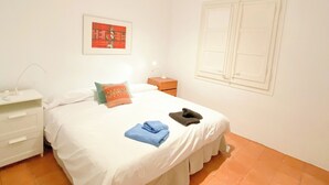 A bedroom with a bed, a nightstand, a dresser, a wall-mounted light, and a window with blinds.