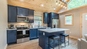 A modern kitchen with dark cabinets, stainless steel appliances, and a central island with bar stools. - The Falcons Nest- Hot Tub - Fire Pit - Large Covered Porch (Bryson City)