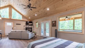 A spacious room with a large bed, a sofa, a fireplace, and a ceiling fan. - The Falcons Nest- Hot Tub - Fire Pit - Large Covered Porch (Bryson City)