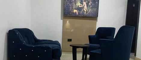 Una sala de estar moderna con dos sofás azul oscuro, una mesita redonda y un cuadro abstracto grande en la pared.