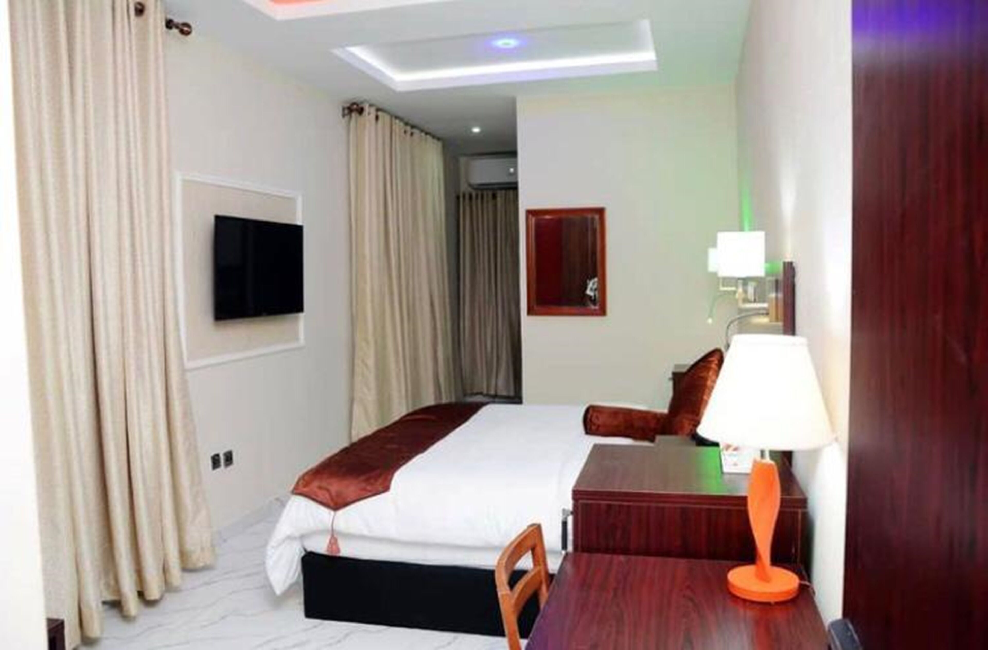 Une chambre d’hôtel équipée d’un lit, d’un bureau, d’une chaise, d’un téléviseur fixé au mur et d’une lampe.
