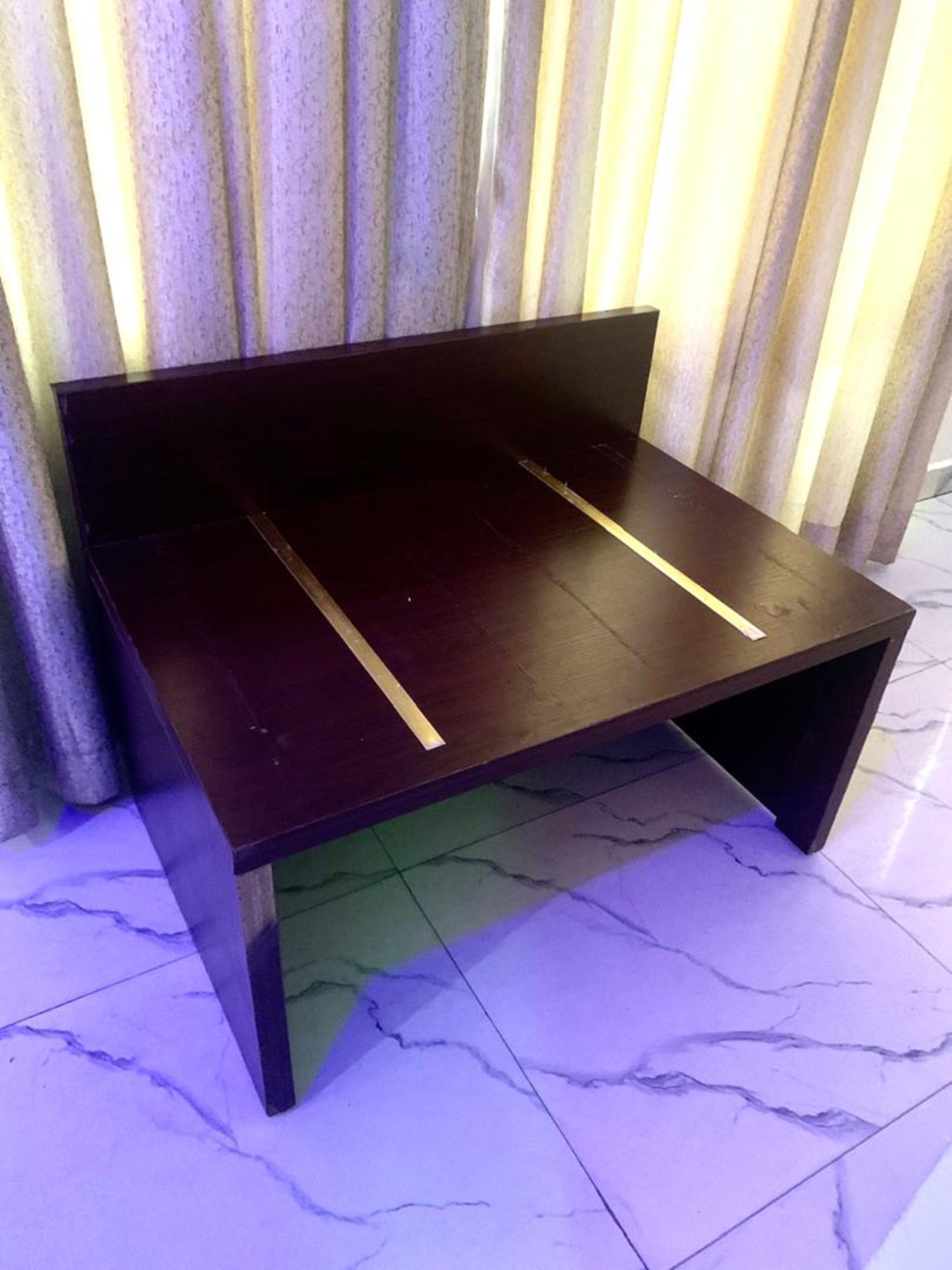 A dark wooden bench with a simple design, positioned against a striped curtain backdrop.