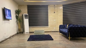 Una sala moderna con un sofá azul oscuro, un televisor de pantalla plana y un equipo de aire acondicionado grande.