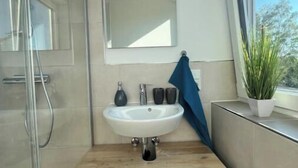 Een moderne badkamer met een douchecabine van glas, een witte wastafel en een houten opbergmeubel met lades.